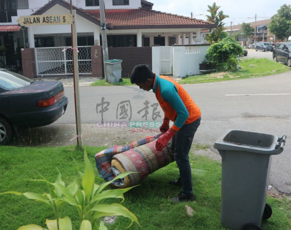 清洁工人将丢在路旁的床褥垃圾收走。