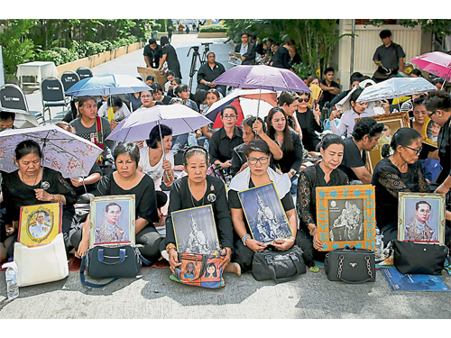 曼谷詩麗拉醫院外一批民眾在泰王蒲湄蓬移靈前，手持泰王遺照跪地致哀。（歐新社）