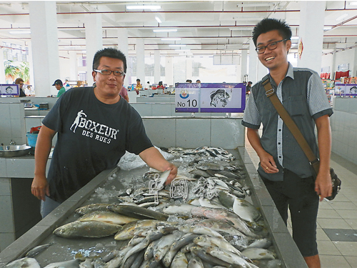 顧客在海產攤格，選擇魚類。左為張振成。