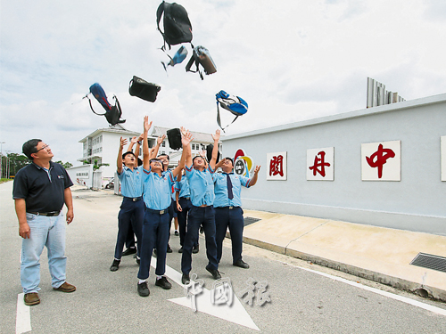 蔡若峰（左）在關丹中華中學校門，見證考生們歡快地以拋書包慶祝統考結束。