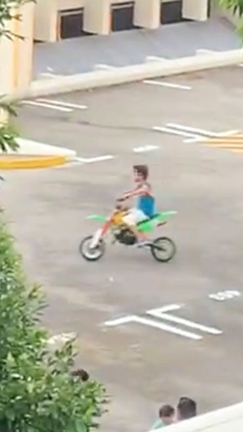 小男生骑着青白色的迷你越野摩哆，在停车场顶层来回奔驰。