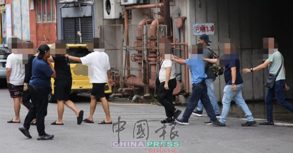 男顾客们从大厦的地下泊车场离开，准备上警车。